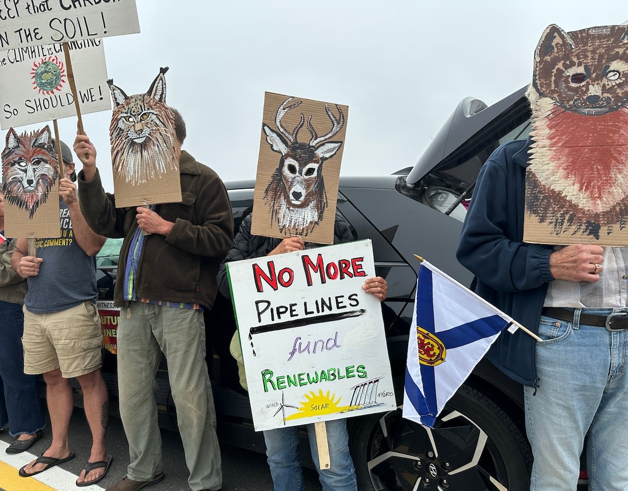 A group of people with hand-drawn masks of animals over their faces hold protest signs reading "No more pipelines, fuel renewables."