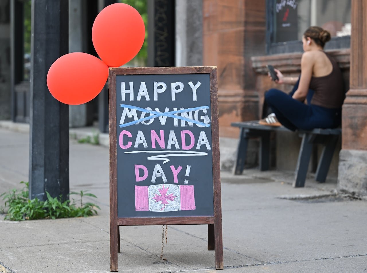 default-4718 A black chalk sign says, "HAPPY CANADA DAY!" The word "moving" has been crossed out.