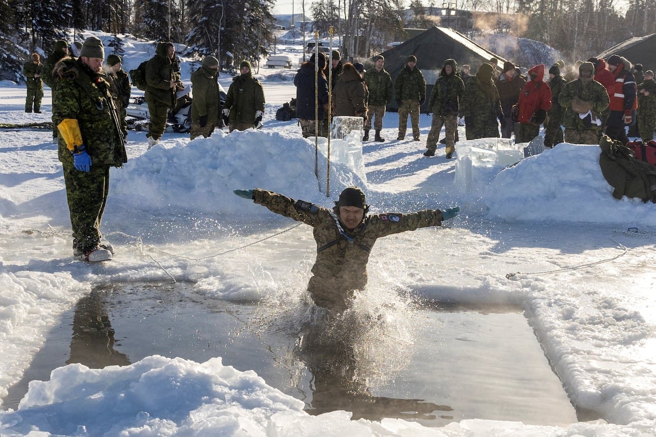 Army reserve person jumps into ice waters with other colleagues watching outside in the cold.